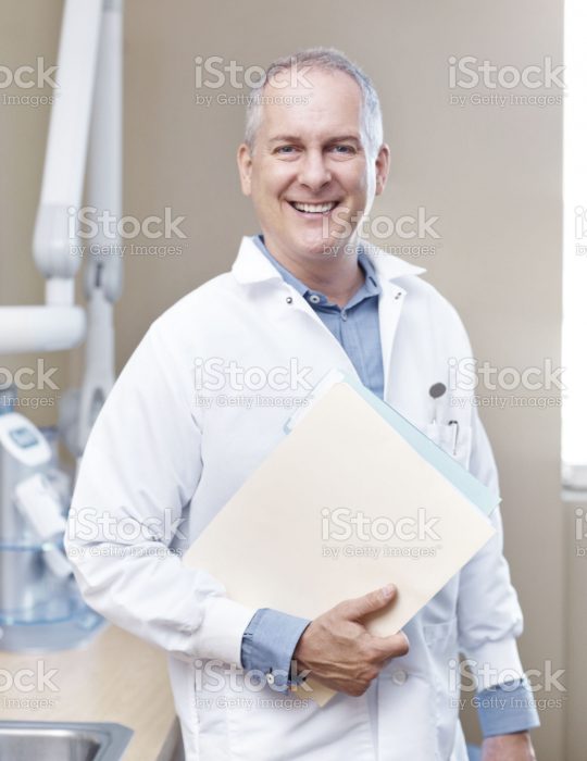 A mature dentist holding a patient's chart and smiling at the camera - portrait